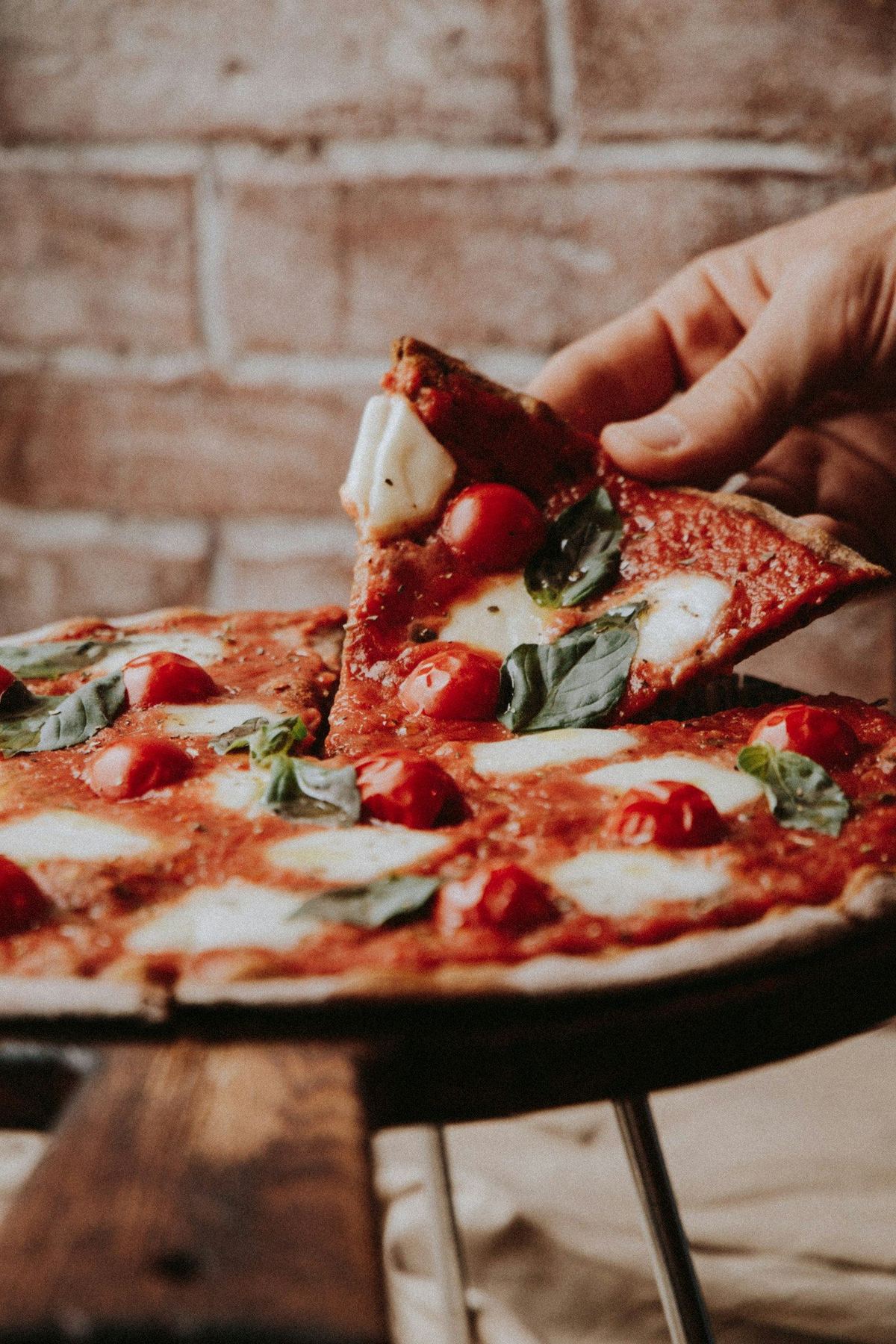 Part de pizza tenue à la main devant un mur de briques
